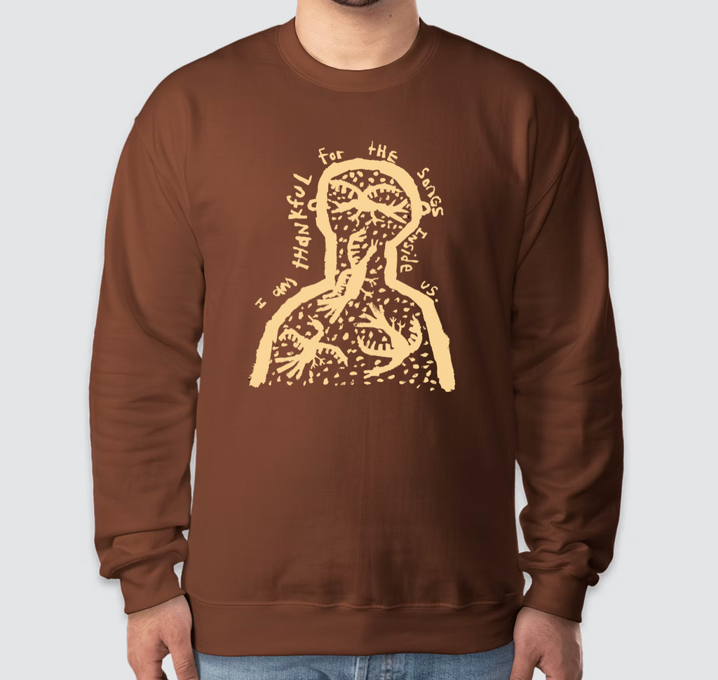 A person wearing a brown crewneck sweatshirt with a tan graphic of a human figure and the text 'I am thankful for the eyes' on the front, shown against a light gray background.